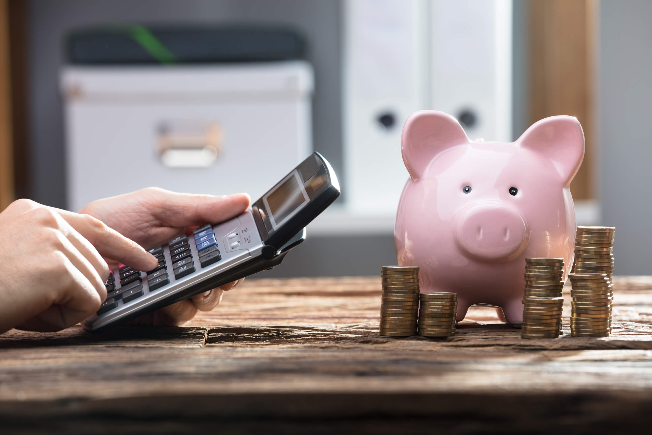 a person using a calculator and a pink piggy bank