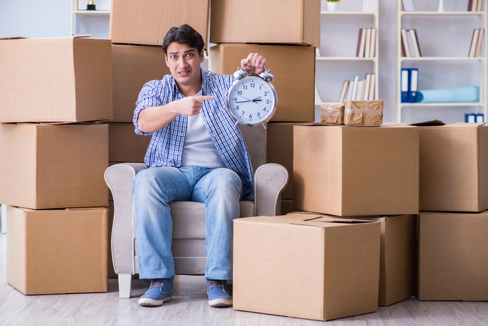 A stressed-out man sitting among new boxes pointing at a clock