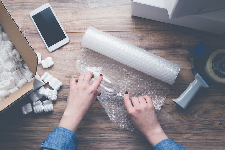 Woman packing a piece of stemware with bubble wrap