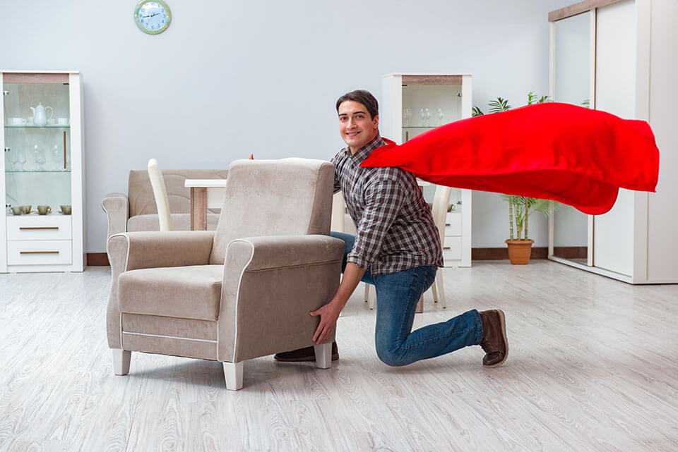 A man with a cape about to lift an armchair