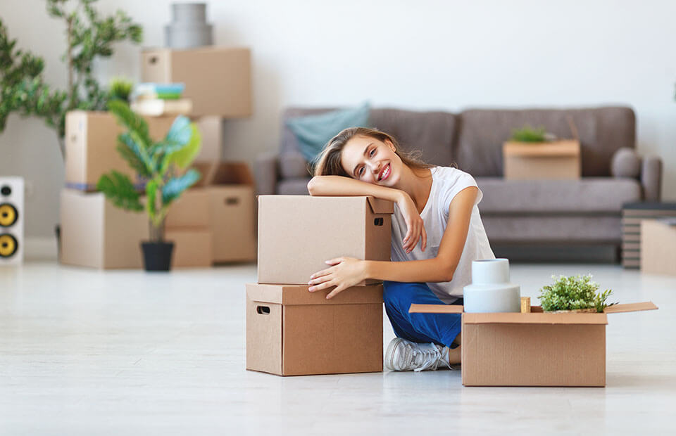 Girl sitting on the floor, leaning on packages, and smiling after hiring a moving company