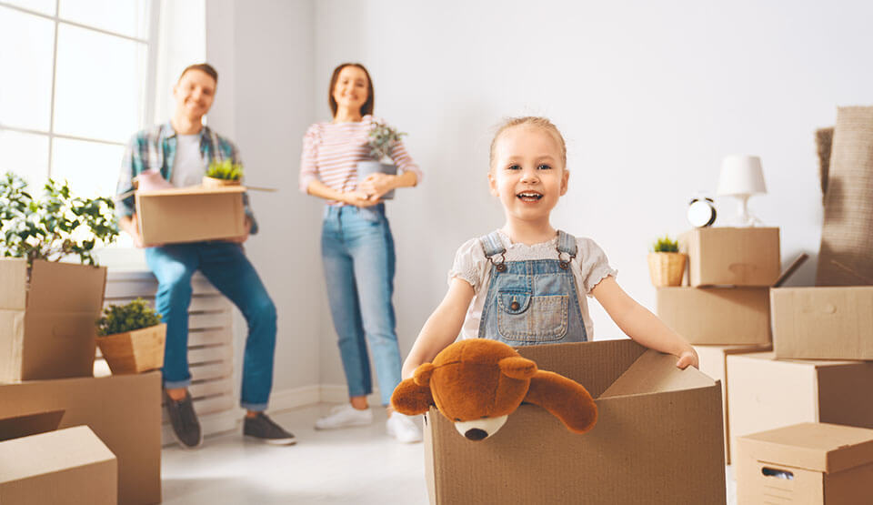 Little girl holding a package with a teddy bear, parents standing behind her