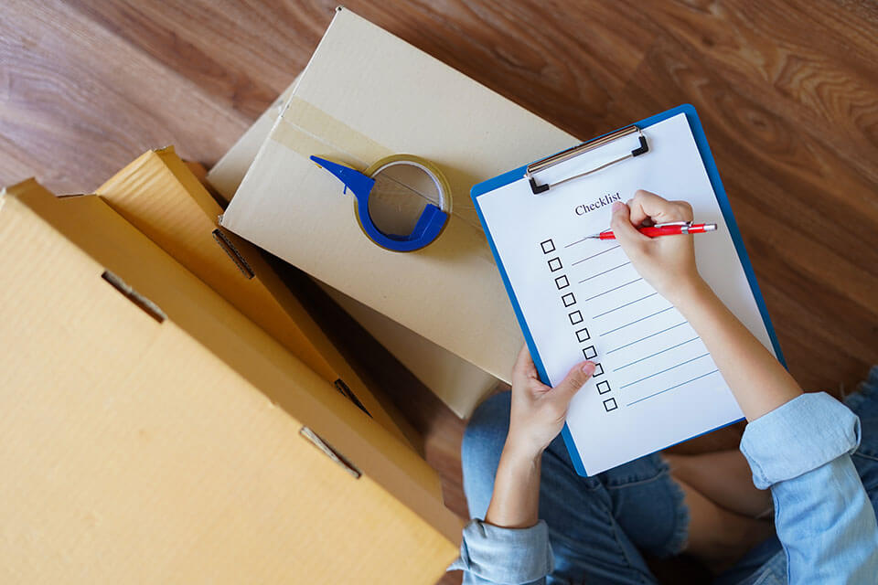 Person holding a pen and a checklist, standing next to packages