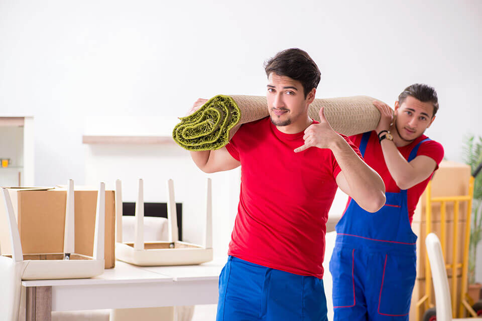 Two movers from a moving company carrying a rolled carpet