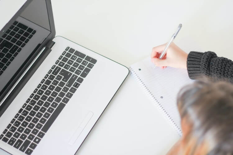 Woman writing in a notebook, looking at a moving company app