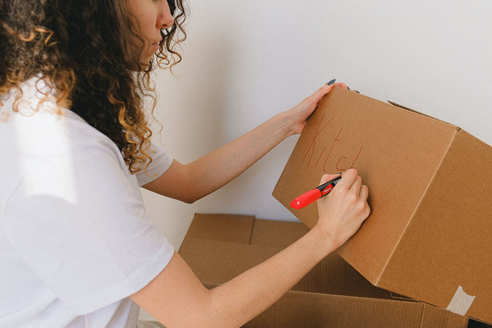 A woman labeling a box after using a moving app to find a moving company