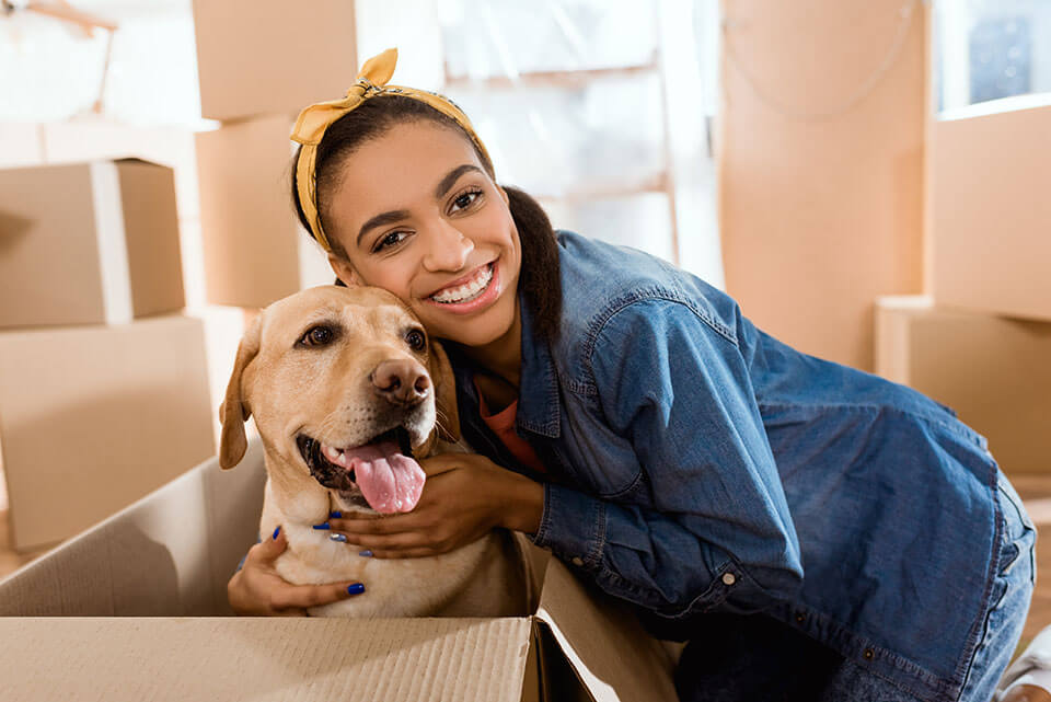 A smiling girl hugging a golden retriever in the box, packages behind them