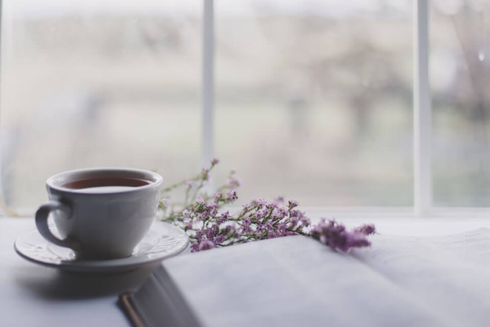 A cup of tea, book, and flowers on the white surface