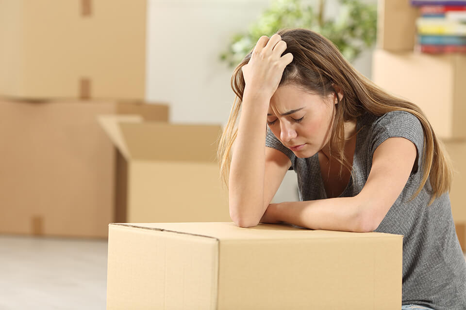 A worried woman holding her head and leaning on a box, surrounded by boxes